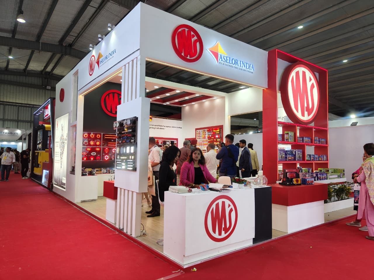 WAS and Aselor India corner stall with WAS logo, red shelving wall and visitors at the counters