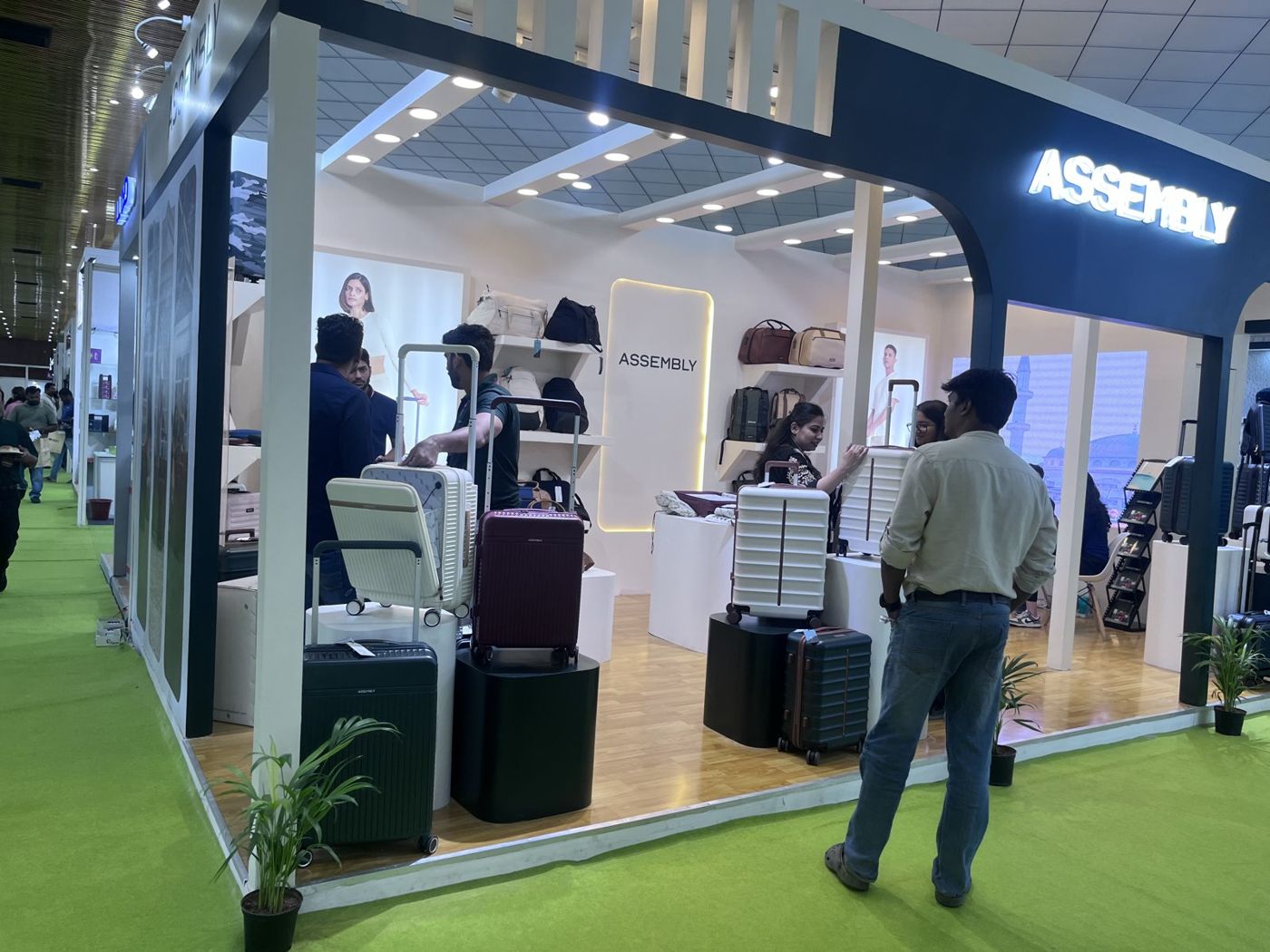Inside the Assembly stall with backlit brand panel, bag shelves, plinths and timber-look floor