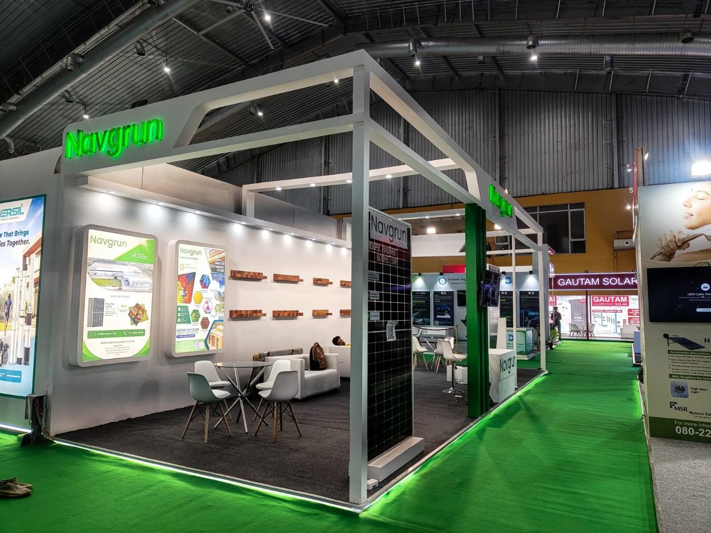 White open-frame corner stall with green backlit lettering, a solar module display and a green LED lit platform edge