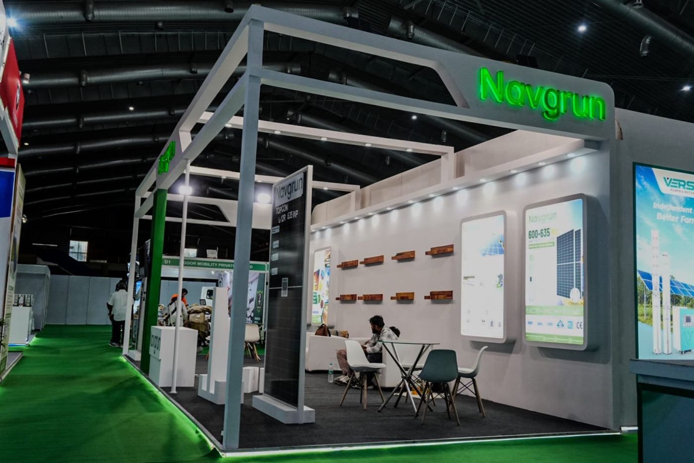 Side of the open-frame stall with a solar module display, wall lightboxes and glass meeting tables