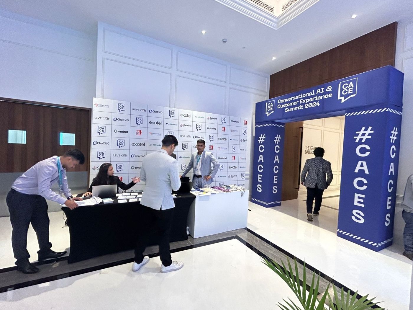 Registration desks in front of the CACES sponsor logo wall, with the blue entry arch to the right