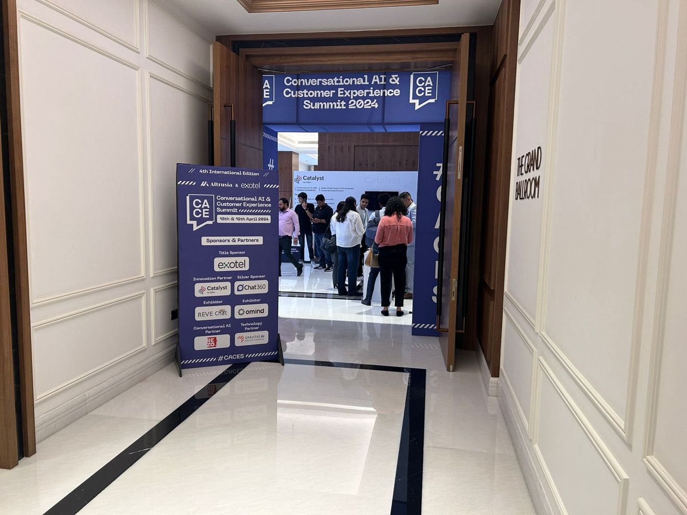 Second CACES arch framing the ballroom doors, with a sponsors and partners standee in the corridor