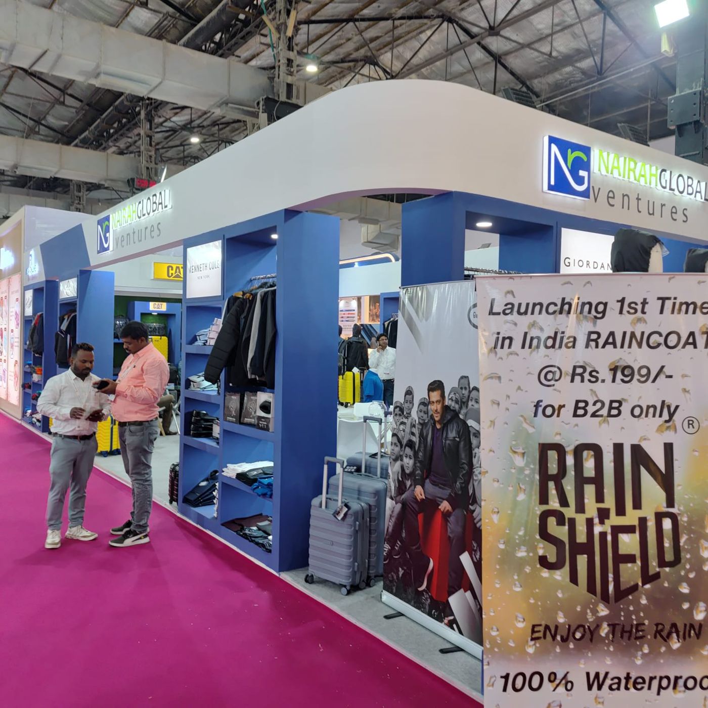 Global Ventures stall with curved white fascia, backlit logo and blue display bays holding jackets and suitcases