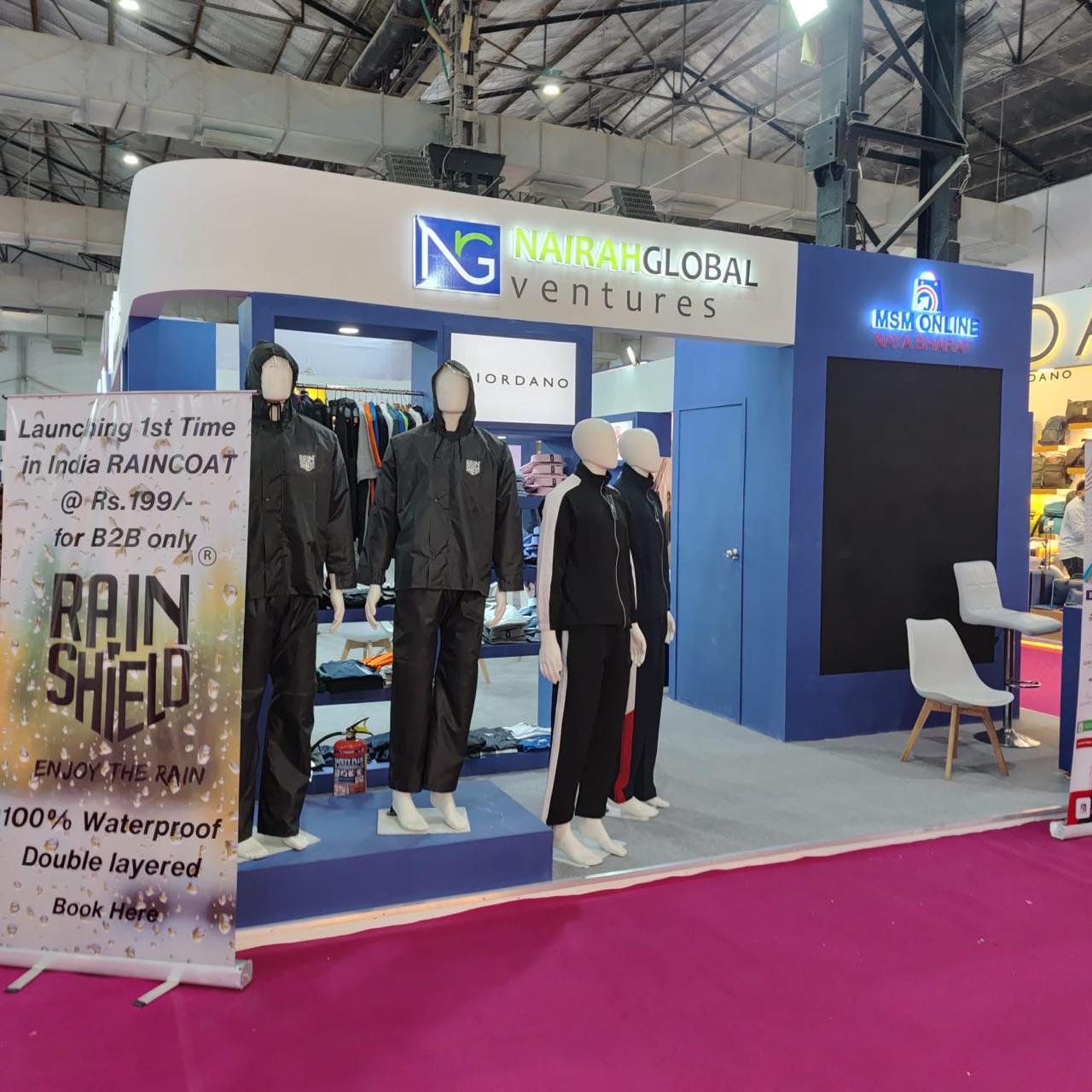 Corner of the Global Ventures stall with mannequins in black raincoats on a blue plinth and a lit MSM Online logo