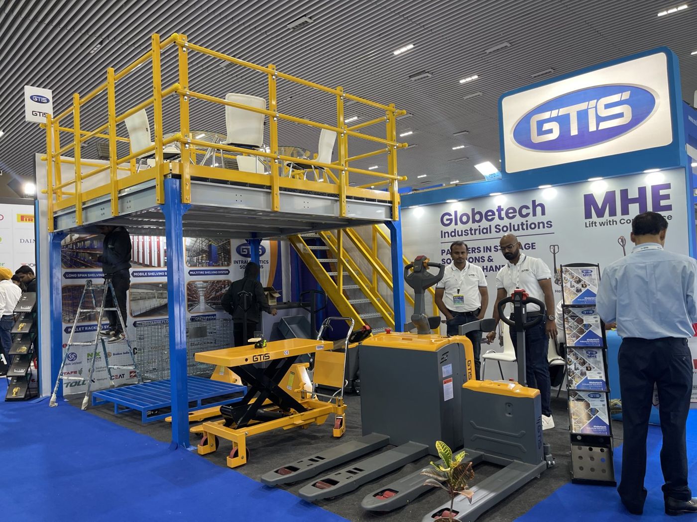 GTIS Globetech two-level stall with blue steel columns, yellow railings and pallet trucks below