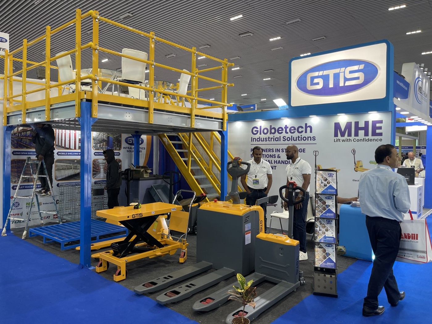 Electric pallet trucks and scissor lift table under the GTIS deck with shelving graphics behind