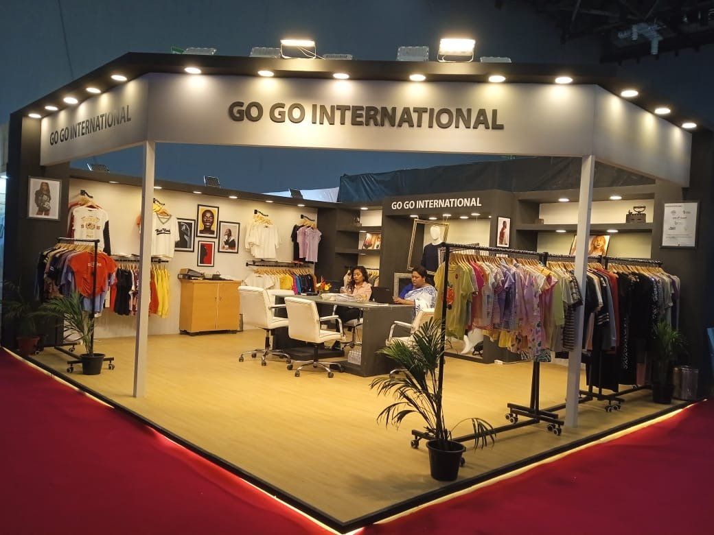 Go Go International apparel stall with grey fascia, downlights, garment rails and meeting table on a raised platform