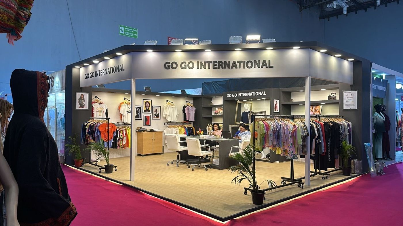 Wide view of Go Go International stall on a raised platform with LED edge strip and potted palms