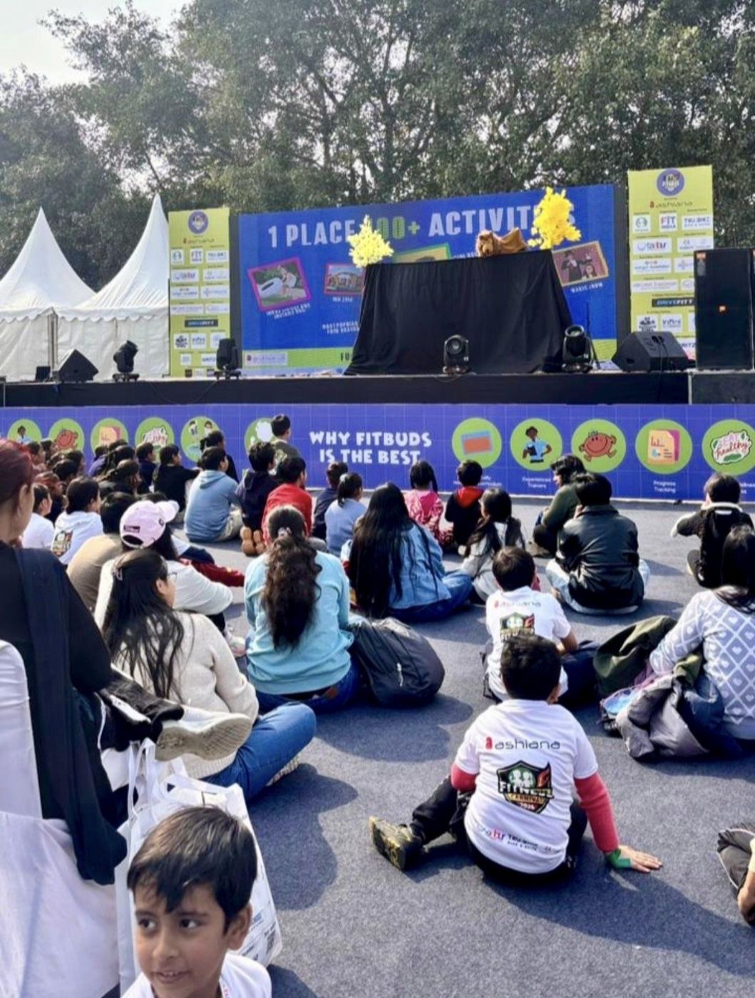 Families seated on carpet facing the stage, with an illustrated printed fascia along the stage front