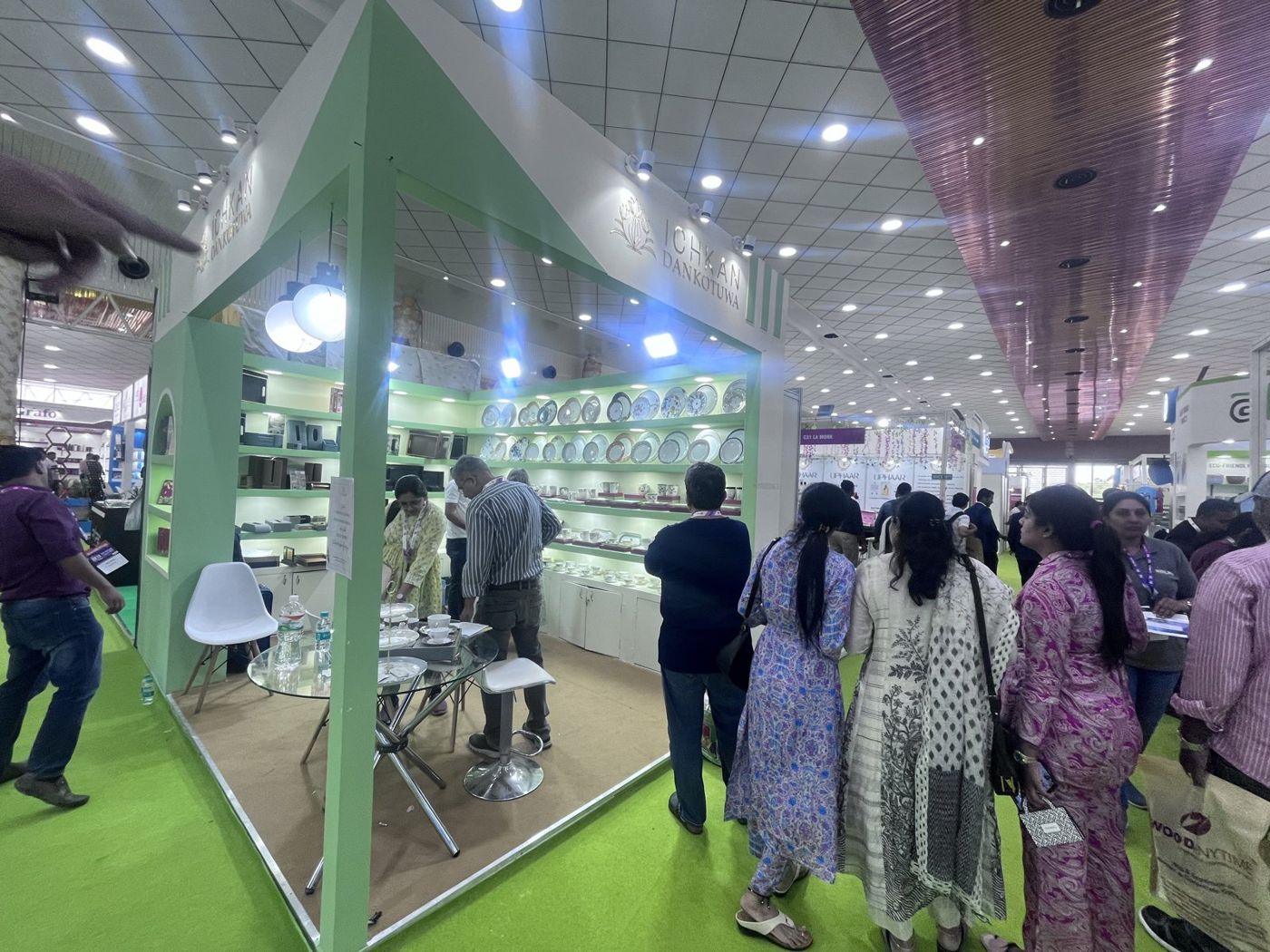 Corner view of the green stall with stocked plate shelves and visitors in the aisle