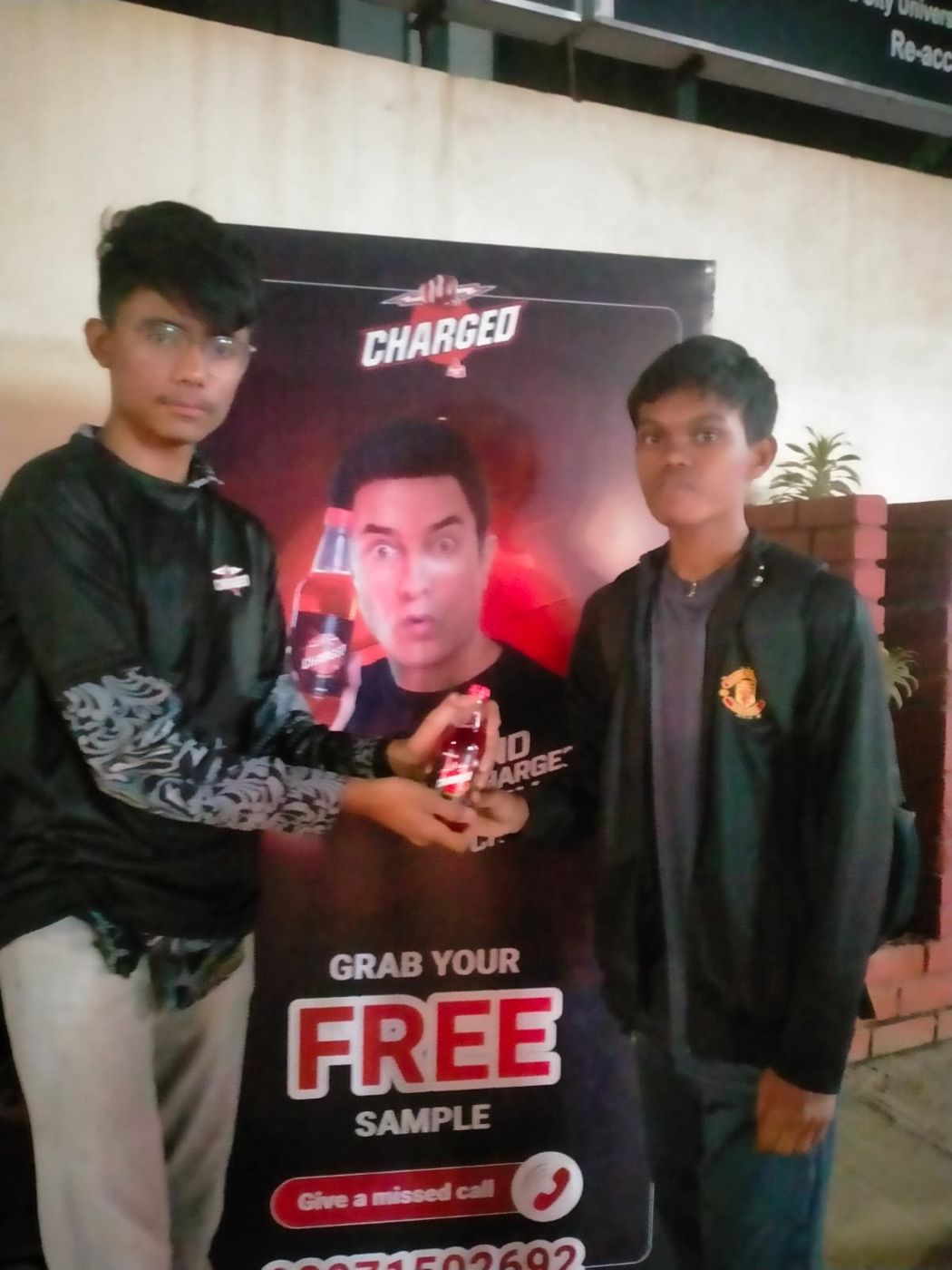 Sample handover to a student in a black jacket in front of the printed beverage backdrop