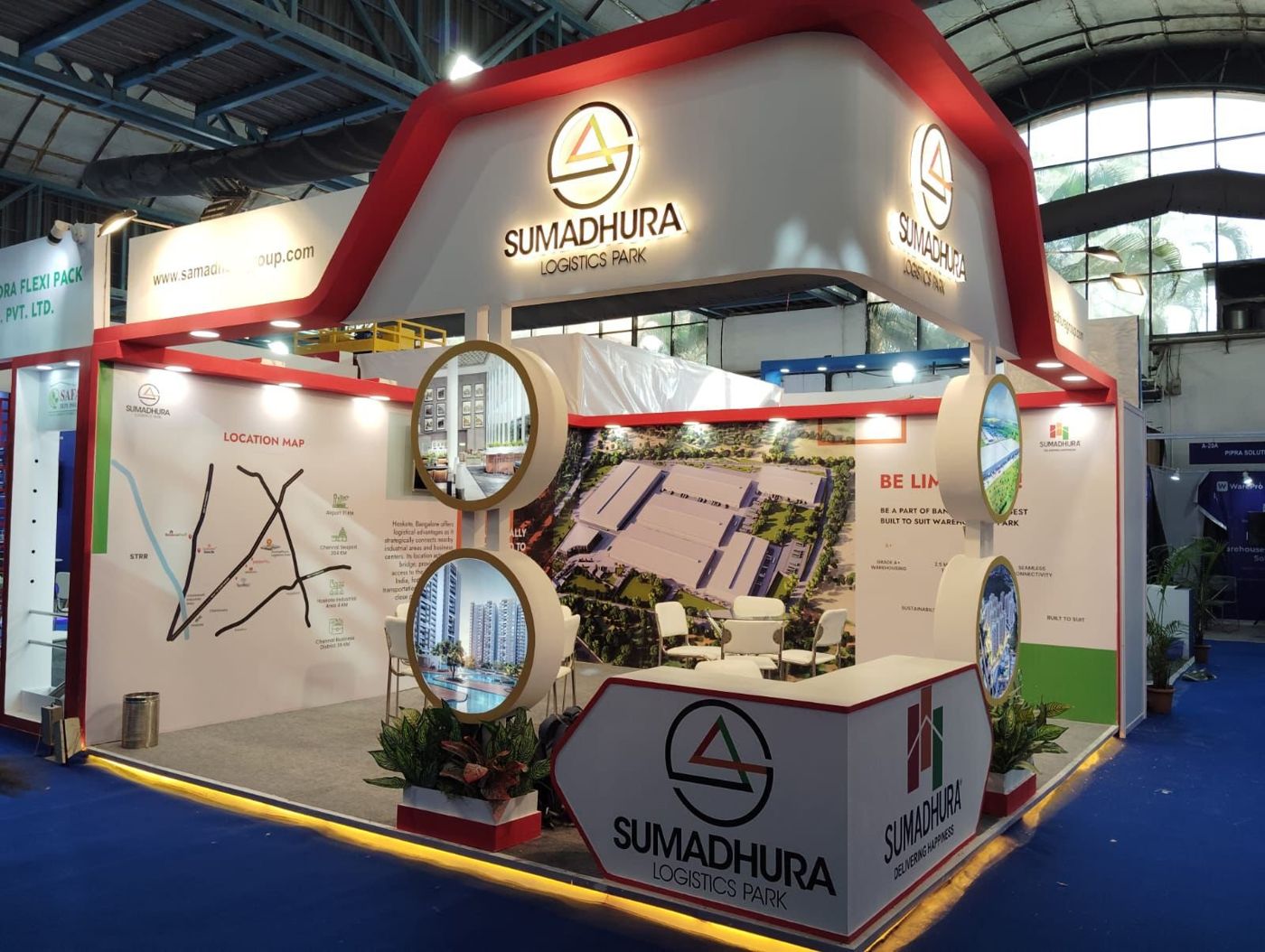 Red and white Sumadhura Logistics Park stall with arched fascia, backlit logos and round lightboxes