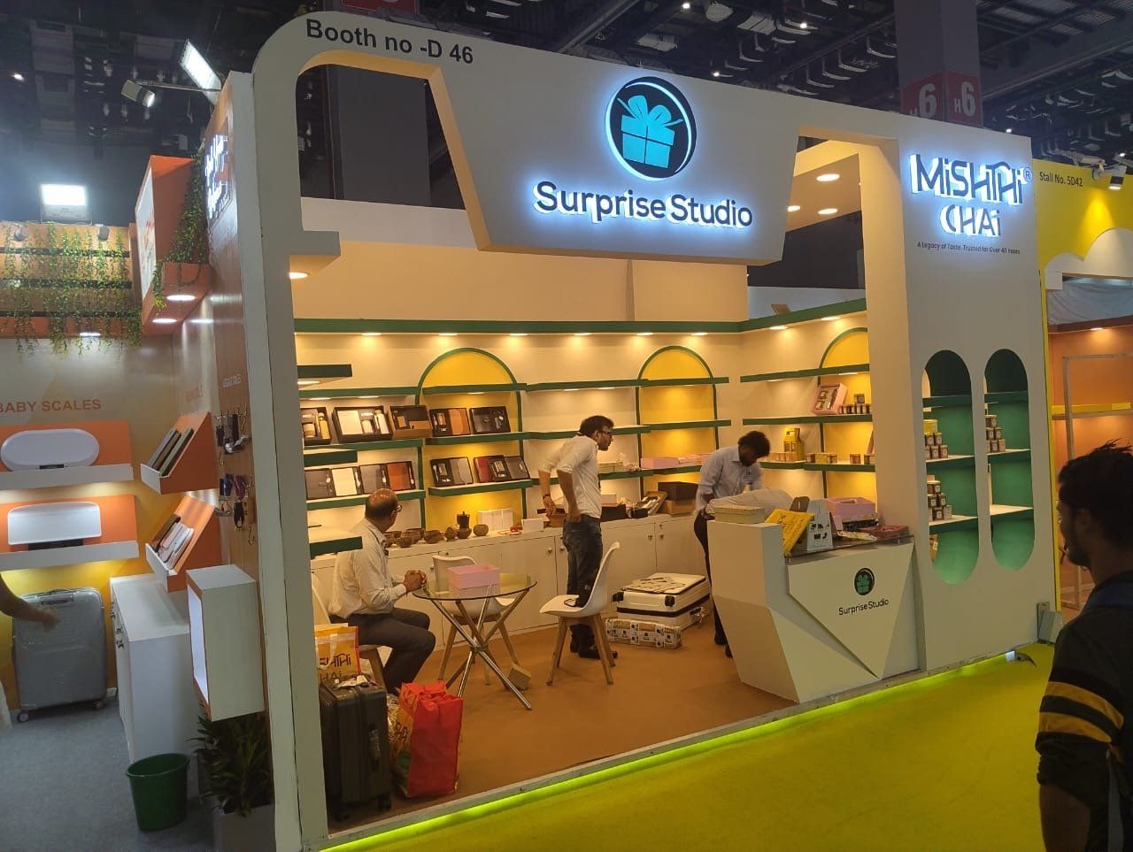 Surprise Studio and Mishthi Chai stall with backlit logos, green-edged shelves and arched yellow niches