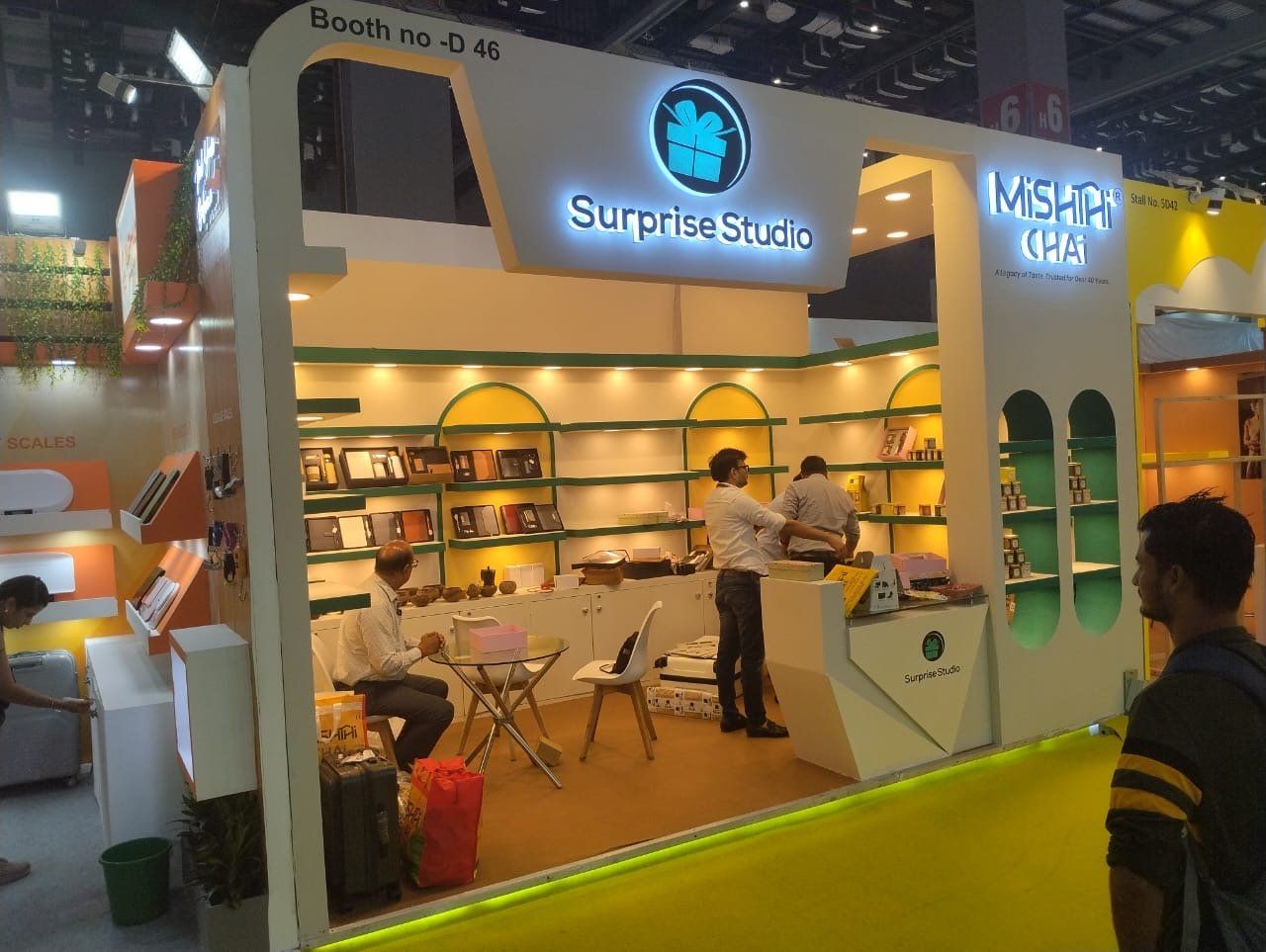 Inside the Surprise Studio stall with gift sets on lit shelves, yellow arches and an angled counter