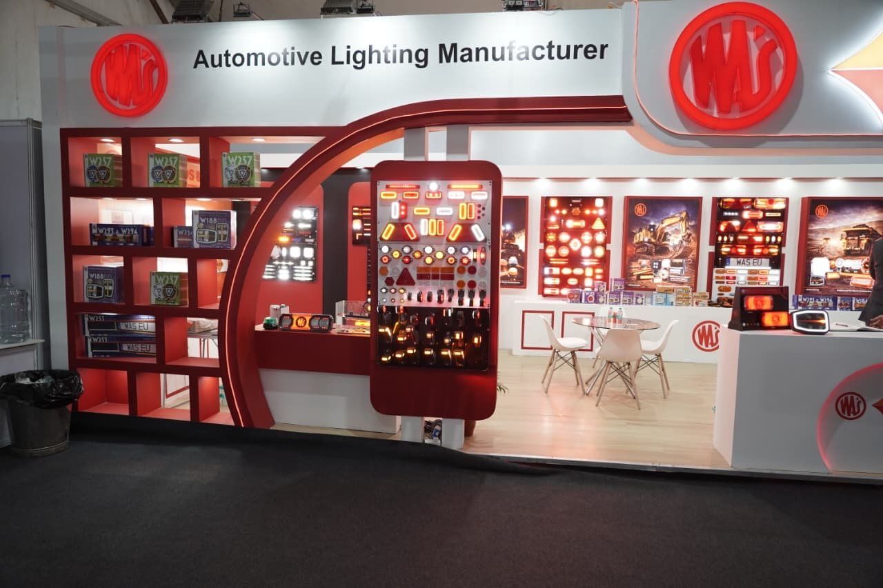 WAS stall seen from the aisle with backlit red logos on a white fascia and a lamp display panel