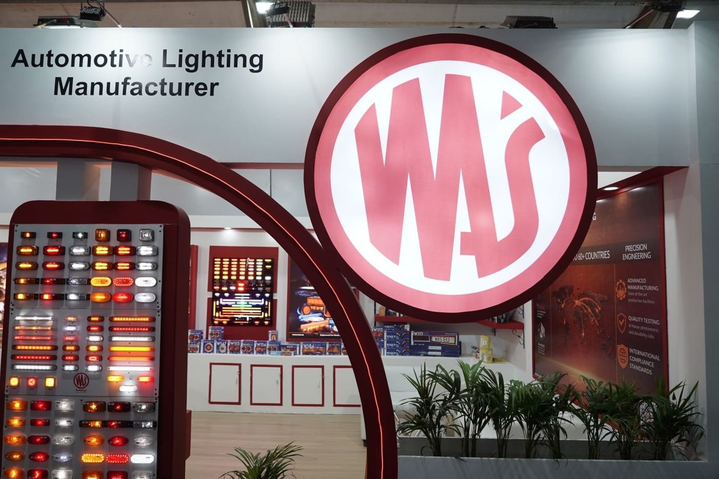 Large backlit circular WAS logo inside the red arch, with lit lamp boards and planters behind