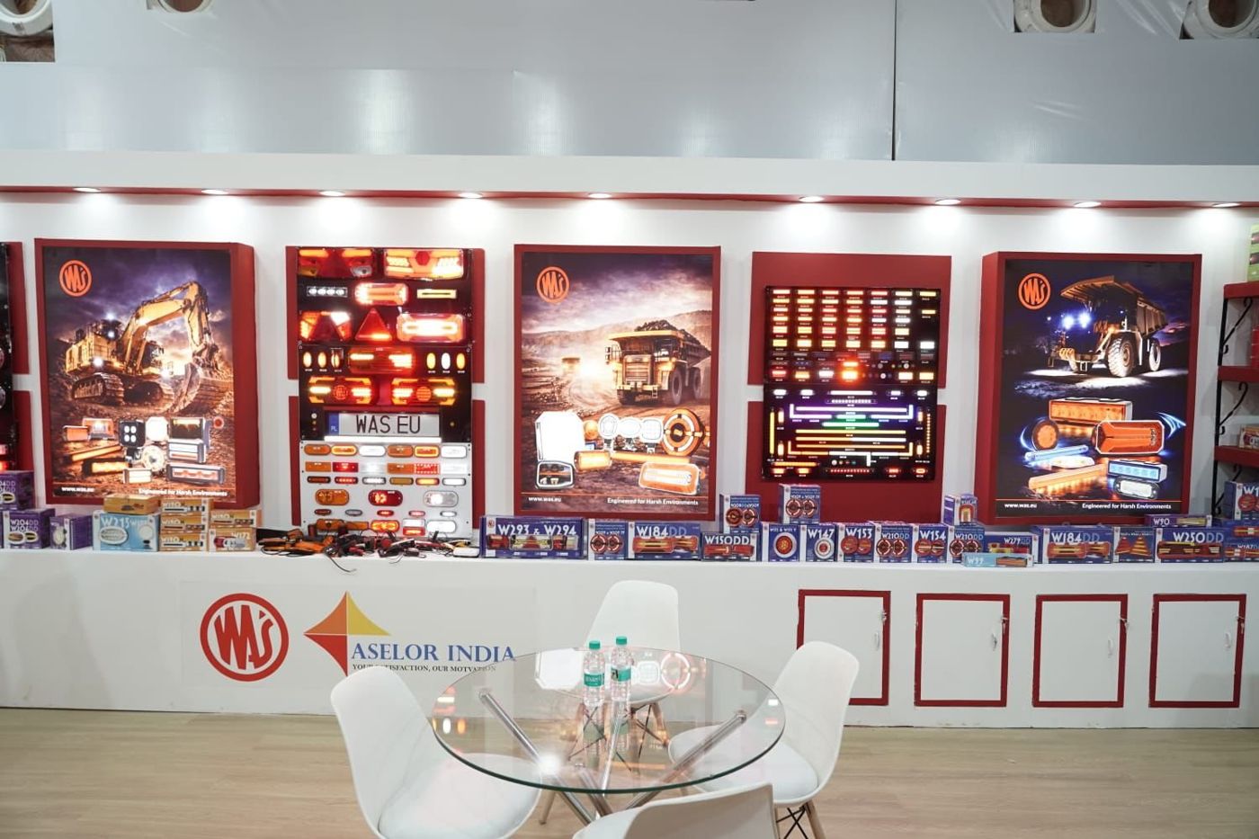 Back wall of the WAS stall with lightbox posters, lamp boards, boxed stock and a glass meeting table